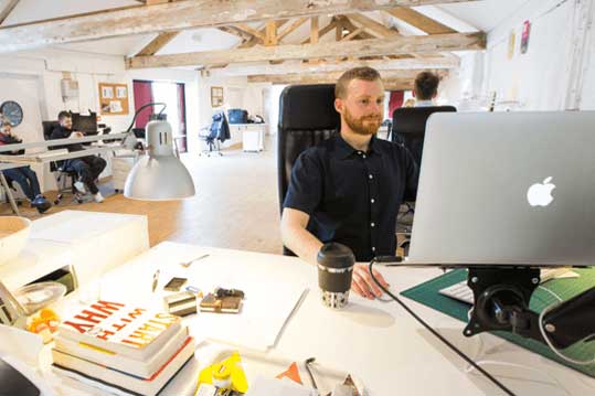 Working man on an Apple computer at a desk in an open office.
